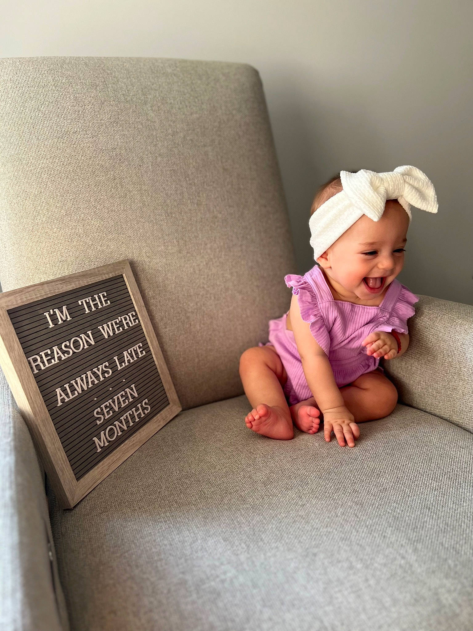 Emilija is registered to the contest to win money with this photo: baby, baby_toddler_clothing, child, comfort, couch, fashion_accessory, floor, flooring, foot, headwear, human_leg, knee, linens, magenta, person, room, sitting, smile, thigh, throw_pillow