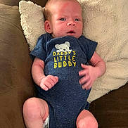 Toby is registered to the contest to win money with this photo: baby, infant, onesie, blue_clothing, pillow, couch, cushion, person, child, newborn, sitting, face, head, skin, hand, footwear, white_socks, expression, indoor, comfortable