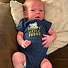 baby, infant, onesie, blue_clothing, pillow, couch, cushion, person, child, newborn, sitting, face, head, skin, hand, footwear, white_socks, expression, indoor, comfortable