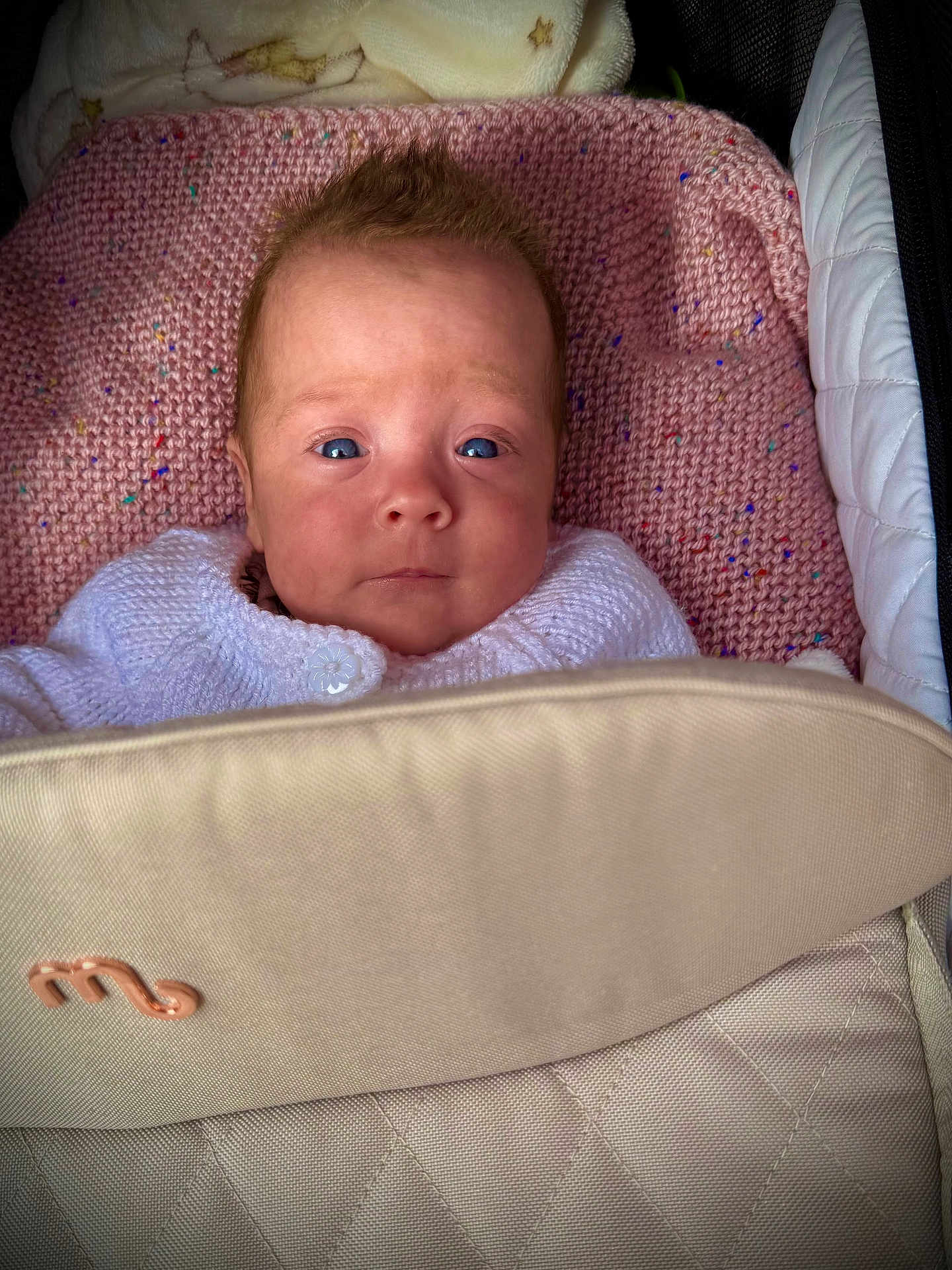 Esmae is registered to the contest to win money with this photo: baby, infant, face, blue_eyes, knitwear, blanket, pink_blanket, stroller, beige, closeup, portrait, child, young, cozy, warm, expression, person, indoor, cute, newborn
