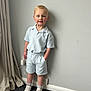 child, boy, smile, standing, indoor, clothing, shorts, shirt, sneakers, carpet, curtain, wall, hair, face, person, happy, casual, feet, light, room