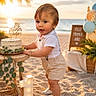 balloons, beach, birthday, cake, celebration, child, greenery, happy, number_one, outdoor, party, plants, sand, shirt, shoes, shorts, sign, sunset, toddler, wooden_table