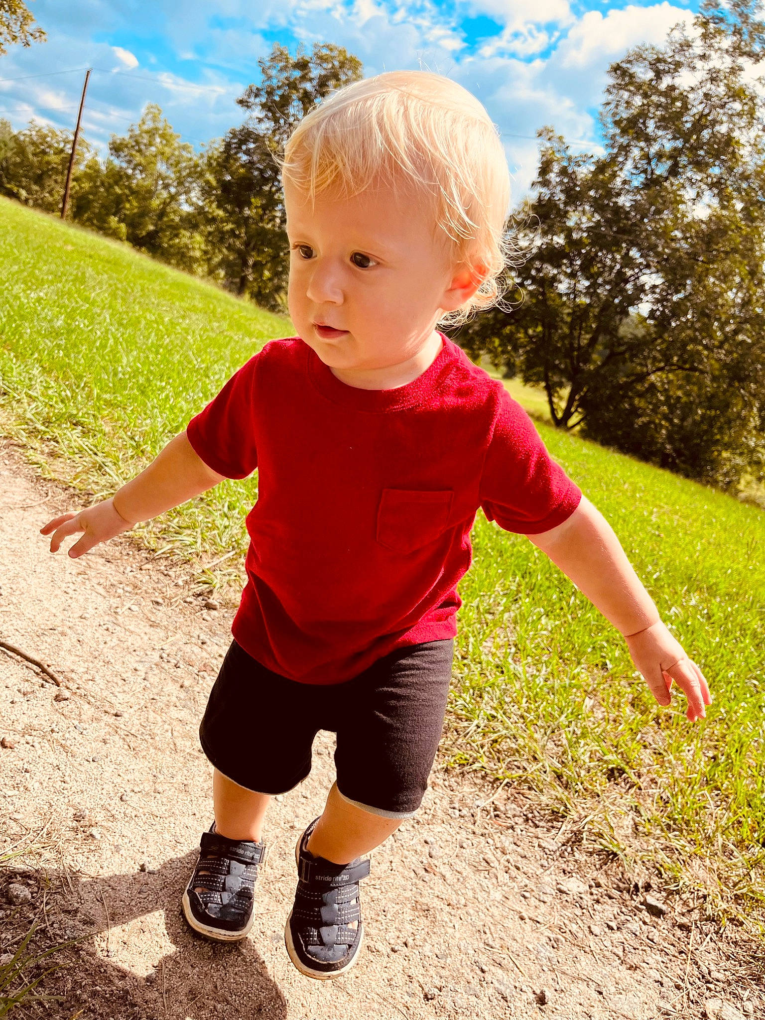 Christian is registered to the contest to win money with this photo: asphalt, cloud, finger, footwear, fun, grass, happy, landscape, leaf, leisure, people_in_nature, person, plant, recreation, shorts, sky, sleeve, standing, summer, toddler