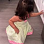 broom, cabinet, chair, child, curly_hair, cute, dress, floor, furniture, hair_tied, indoor, kitchen, person, pink_socks, playful, reaching, squatting, toddler, wooden_floor, young_child