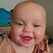 Aniyah is registered to the contest to win money with this photo: baby, smiling, face, child, infant, cute, dress, floral, chubby_cheeks, blue_eyes, indoors, toy, happy, portrait, skin, person, head, clothing, baby_girl, home