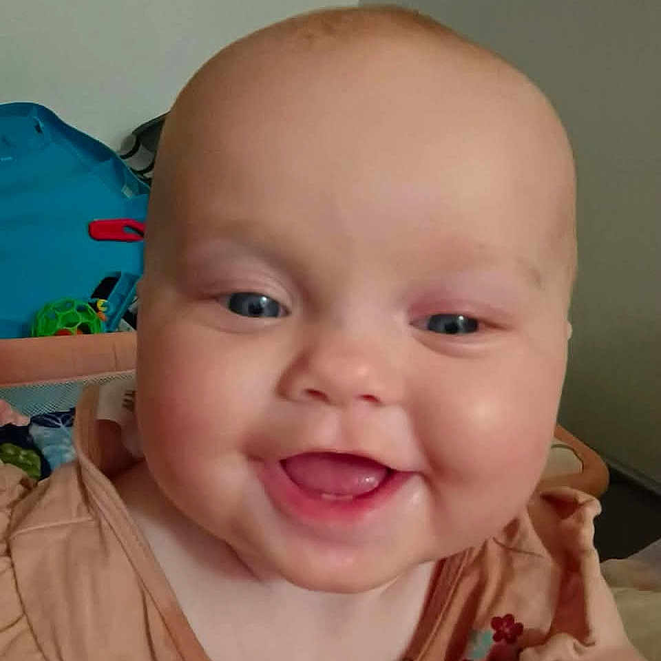 Aniyah is registered to the contest to win money with this photo: baby, smiling, face, child, infant, cute, dress, floral, chubby_cheeks, blue_eyes, indoors, toy, happy, portrait, skin, person, head, clothing, baby_girl, home