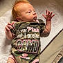 Maggie is registered to the contest to win money with this photo: baby, infant, red_hair, camo_clothing, onesie, hand, face, lying_down, soft_surface, blanket, curious_expression, pink_trim, newborn, skin, person, indoor, portrait, cute, small, child