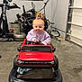 toddler, child, toy_car, red_car, garage, mechanical_parts, concrete_floor, purple_hair_tie, sweater, baby, indoor, vehicle, play, cute, smile, small_car, face, person, head, hands