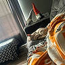 cat, sleeping_cat, pet, animal, couch, blanket, orange_blanket, plush_toys, gnomes, pointed_hats, living_room, home, indoor, sunlight, window, curtains, cozy, relaxing, nap, furniture