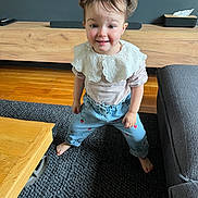 Calie a rejoint le concours — aidez-le/la à gagner de superbes lots ! toddler, child, pigtails, smiling, indoor, carpet, wooden_floor, couch, table, clothing, lace_collar, pants, barefoot, living_room, furniture, person, cute, happy, standing, home