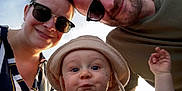 Hugo participe au concours pour gagner de l'argent avec cette photo : family, toddler, child, adult, sunglasses, hat, outdoor, smile, portrait, happy, casual_clothing, face, headwear, striped_shirt, sunlight, sky, parent, baby, closeup, fun