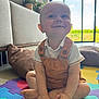 Hugo a rejoint le concours — aidez-le/la à gagner de superbes lots ! baby, child, smiling, indoors, playmat, colorful, overalls, white_shirt, sitting, happy, floor, hands, feet, window, sunlight, plant, cushion, home, portrait, cute