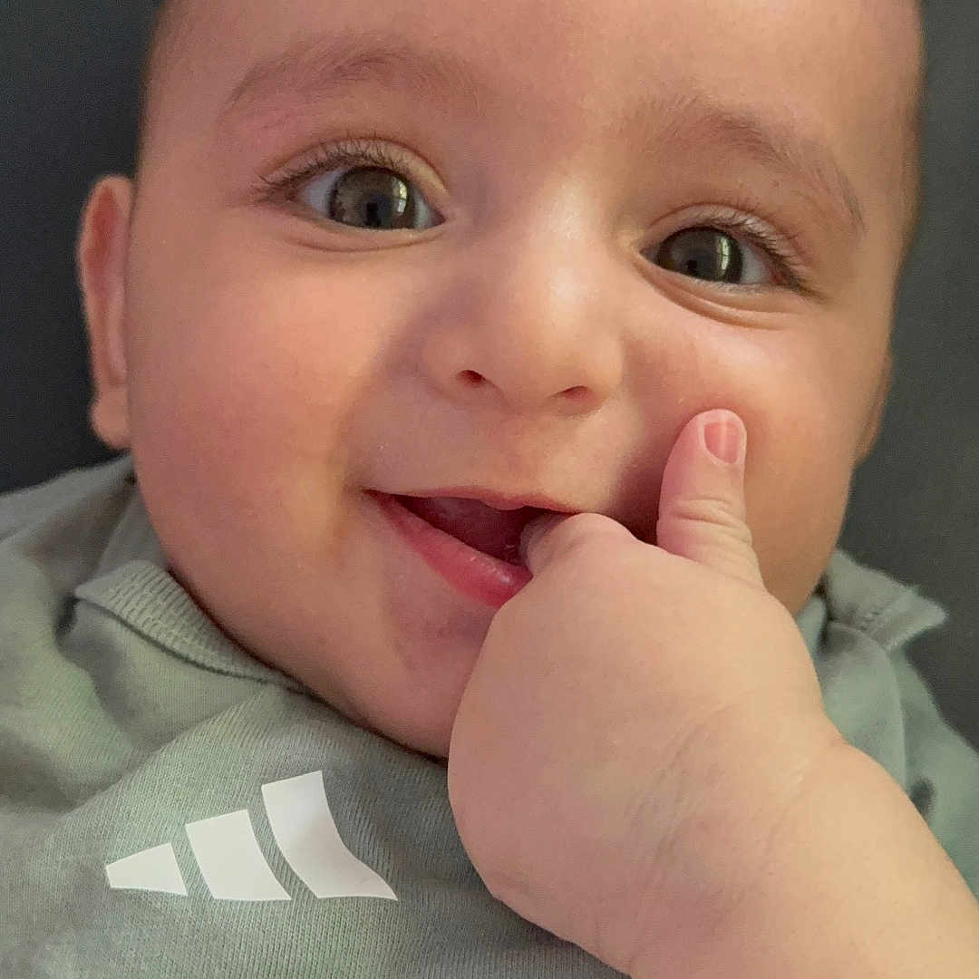Ali joined the competition — help win amazing prizes! baby, child, face, smile, hand, thumb, eyes, cute, infant, portrait, clothing, green_shirt, skin, expression, person, closeup, happy, young, indoors, head
