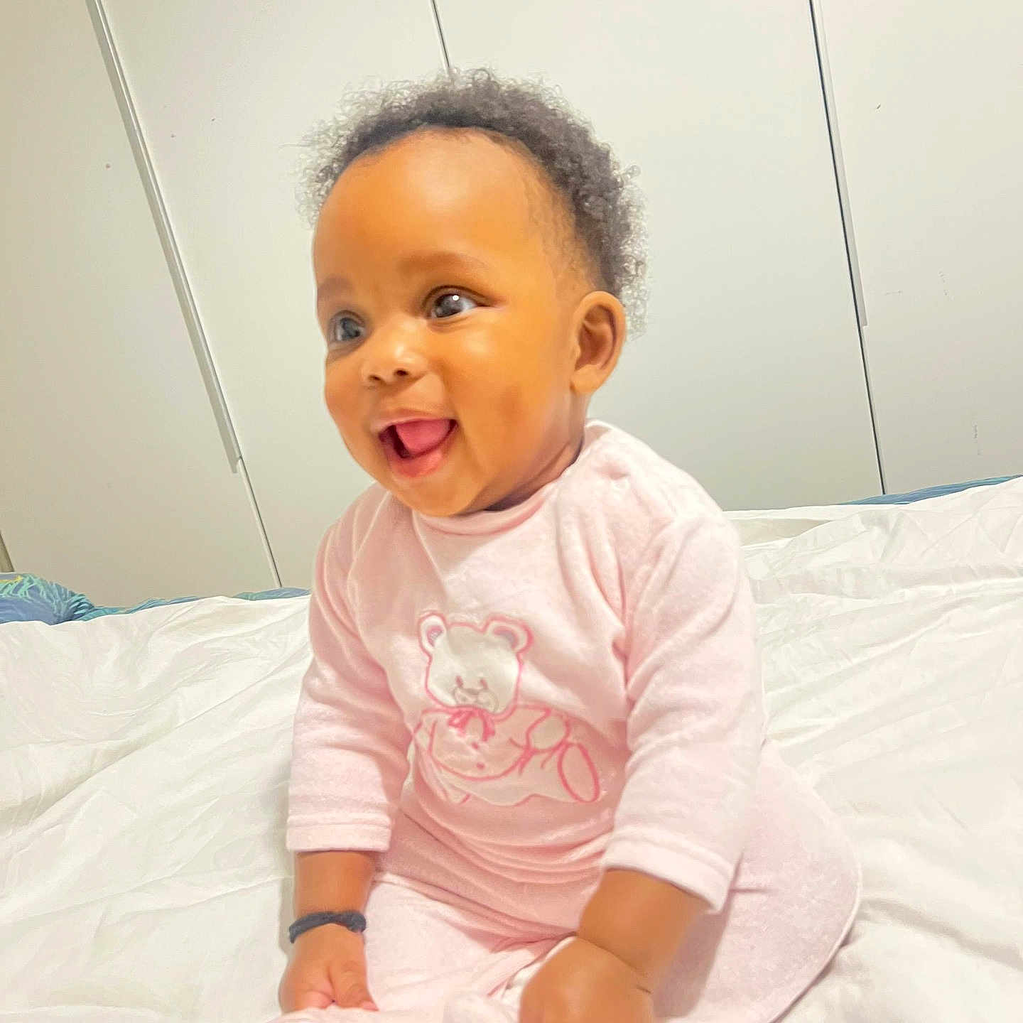 Francesca Gisèle a rejoint le concours — aidez-le/la à gagner de superbes lots ! baby, bed, child, clothing, cozy, curly_hair, cute, face, happy, indoor, infant, person, pink_pajamas, portrait, sitting, sleepwear, smiling, soft_lighting, toddler, white_bedspread