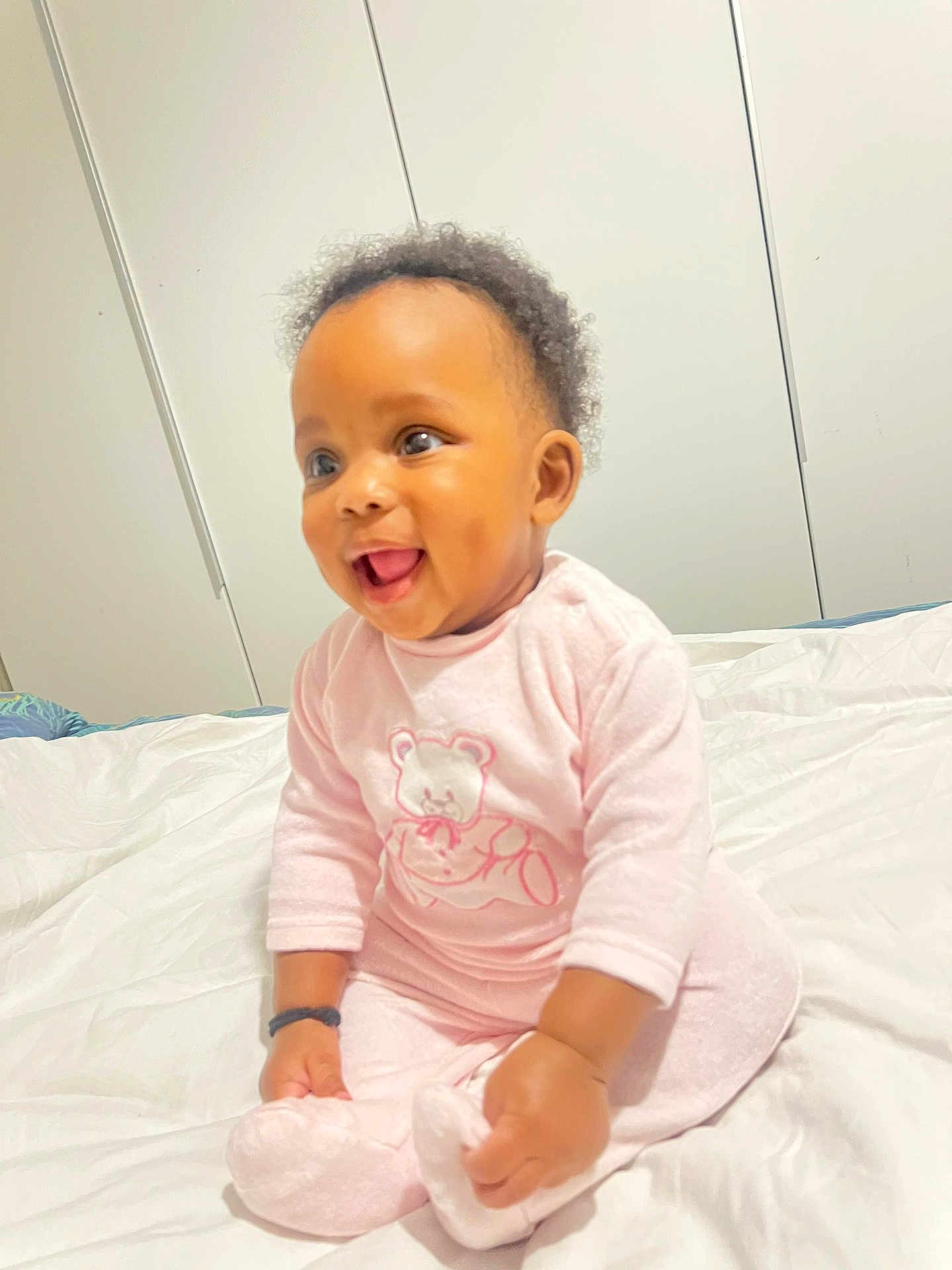 Francesca Gisèle a rejoint le concours — aidez-le/la à gagner de superbes lots ! baby, child, pink_pajamas, smiling, sitting, bed, white_bedspread, indoor, curly_hair, cute, happy, infant, portrait, toddler, person, face, cozy, soft_lighting, clothing, sleepwear