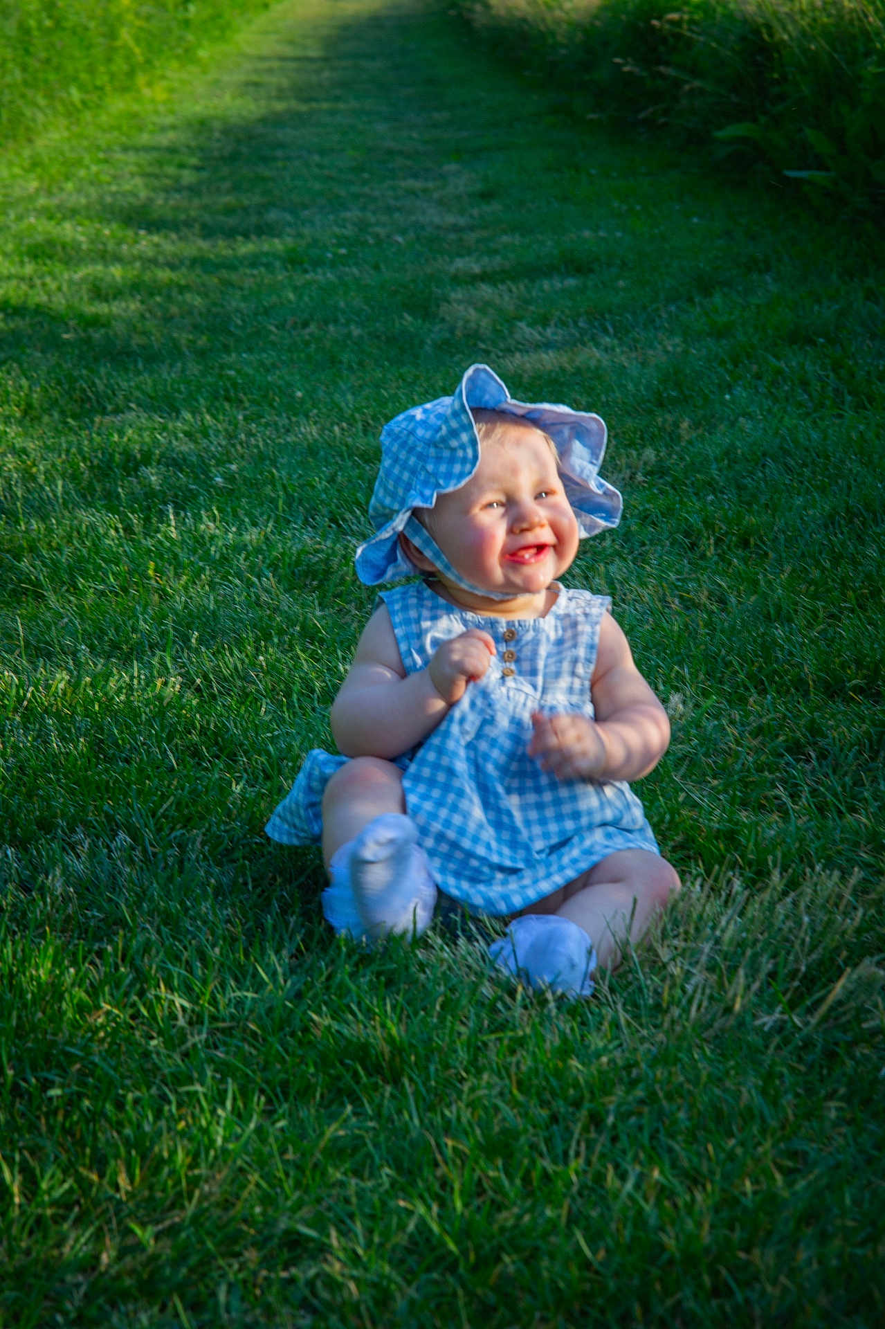 Hailey is registered to the contest to win money with this photo: baby, child, grass, outdoor, smiling, sunhat, blue_dress, happy, sitting, nature, greenery, sunlight, shadow, cute, infant, playful, summer, portrait, young, clothing