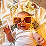 baby, child, sunglasses, white_onesie, blanket, animal_print, carpet, smile, happy, indoor, cute, infant, playful, fashion, accessory, portrait, person, relaxing, fun, light