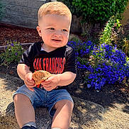 Xander joined the competition — help win amazing prizes! toddler, child, outdoor, flower, plant, rock, leaf, sunlight, shoes, shorts, tshirt, curly_hair, garden, greenery, nature, casual_clothing, sitting, daylight, happy, portrait