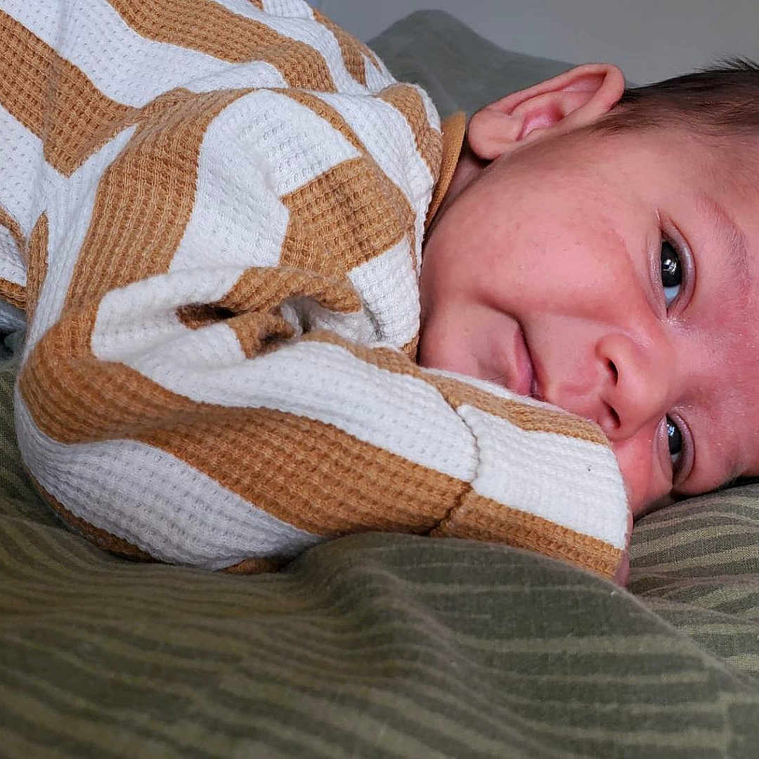 Dragoi joined the competition — help win amazing prizes! baby, bed, brown, child, closeup, cute, face, green_bedspread, head, indoors, infant, newborn, person, portrait, resting, skin, sleepy, soft_texture, striped_clothing, white
