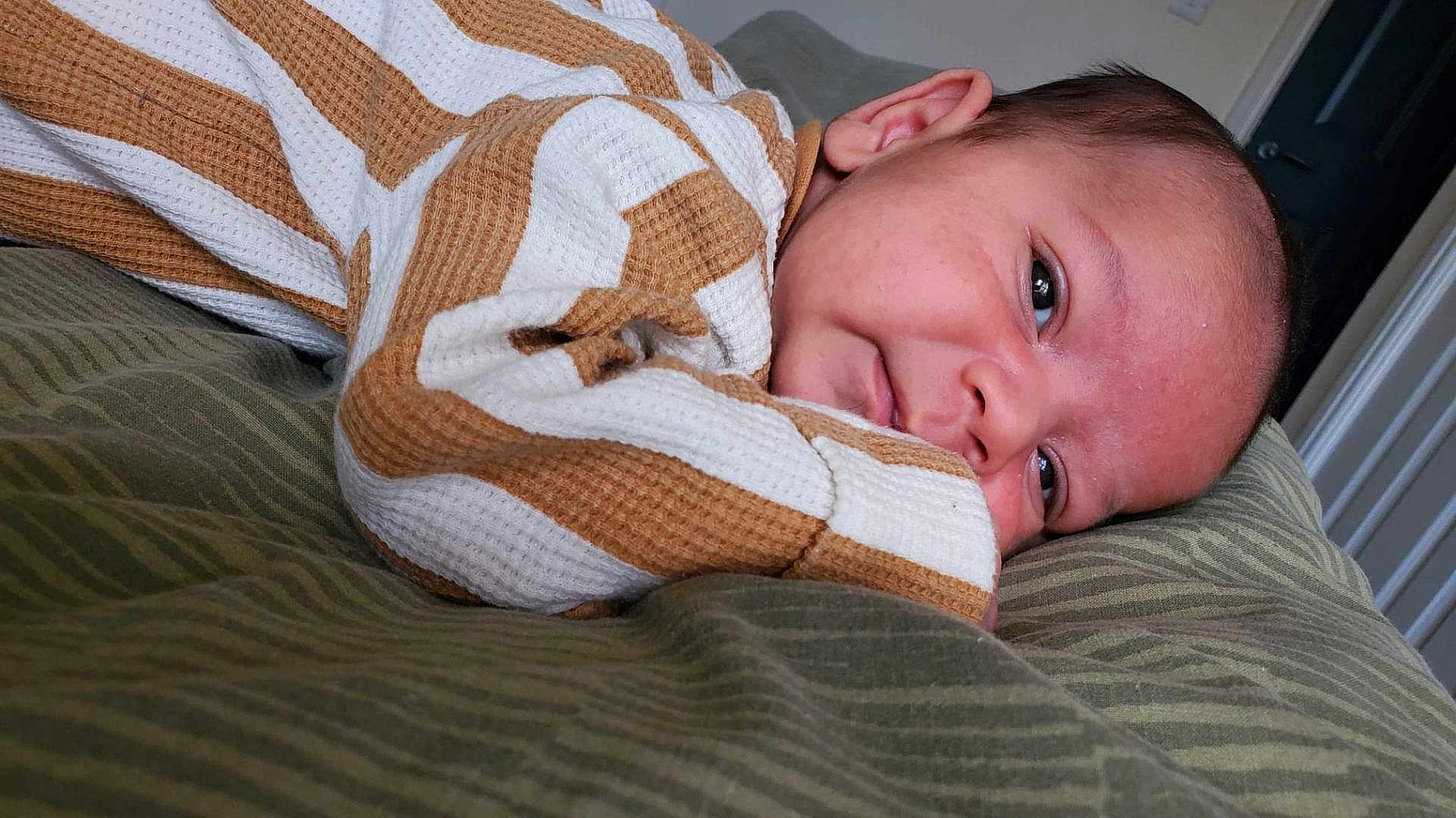 Dragoi joined the competition — help win amazing prizes! baby, infant, face, sleepy, bed, striped_clothing, brown, white, green_bedspread, closeup, person, child, cute, resting, indoors, portrait, soft_texture, newborn, skin, head