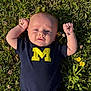 baby, infant, grass, flowers, outdoor, sunlight, blue_shirt, yellow_letter, cute, child, nature, plant, clothing, portrait, person, fist, summer, field, green, happy