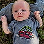 Grayson is registered to the contest to win money with this photo: baby, infant, child, face, person, outdoor, grass, shirt, clothing, cartoon, cherry, graphic, cute, fists, expression, lying_down, striped_cloth, nature, young, portrait