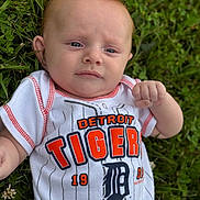 Grayson is registered to the contest to win money with this photo: baby, infant, grass, outdoor, clothing, white_shirt, baseball_jersey, detroit_tigers, person, face, head, blue_eyes, hand, fist, greenery, nature, portrait, young_child, casual, summer