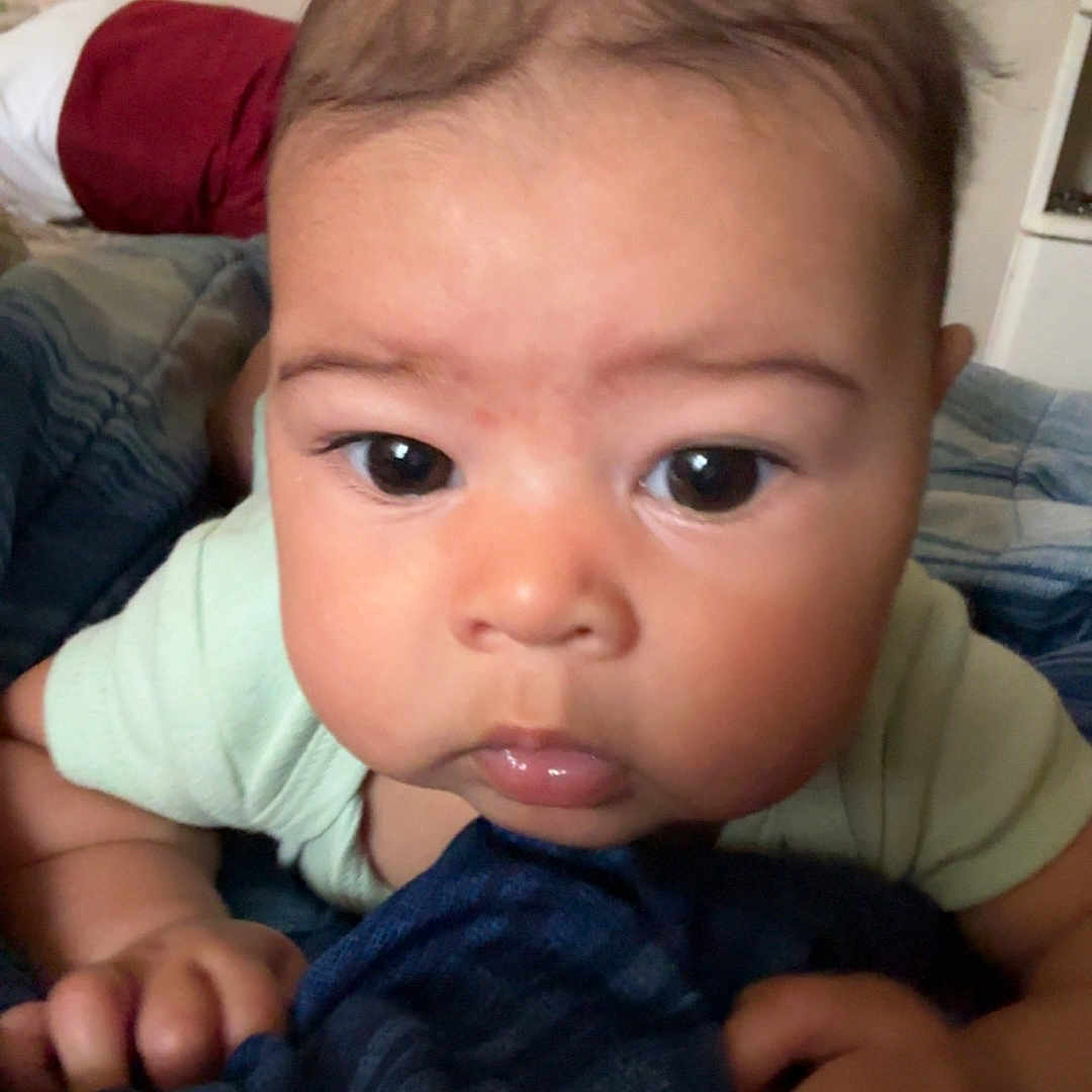 Kaleah is registered to the contest to win money with this photo: baby, child, infant, portrait, face, eyes, wide_eyed, sitting, bed, blanket, bedding, pillow, bedroom, indoor, home, clothing, green_shirt, hands, close_up, photography