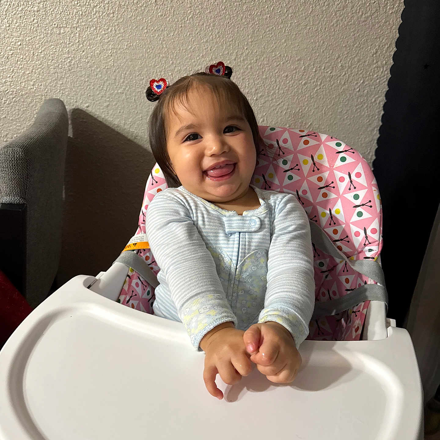 Maleya is registered to the contest to win money with this photo: baby, child, clothing, cute, face, fun, hair_clips, hands, happy, high_chair, indoor, pattern, person, pink, playful, seat, smiling, toddler, tray, wall