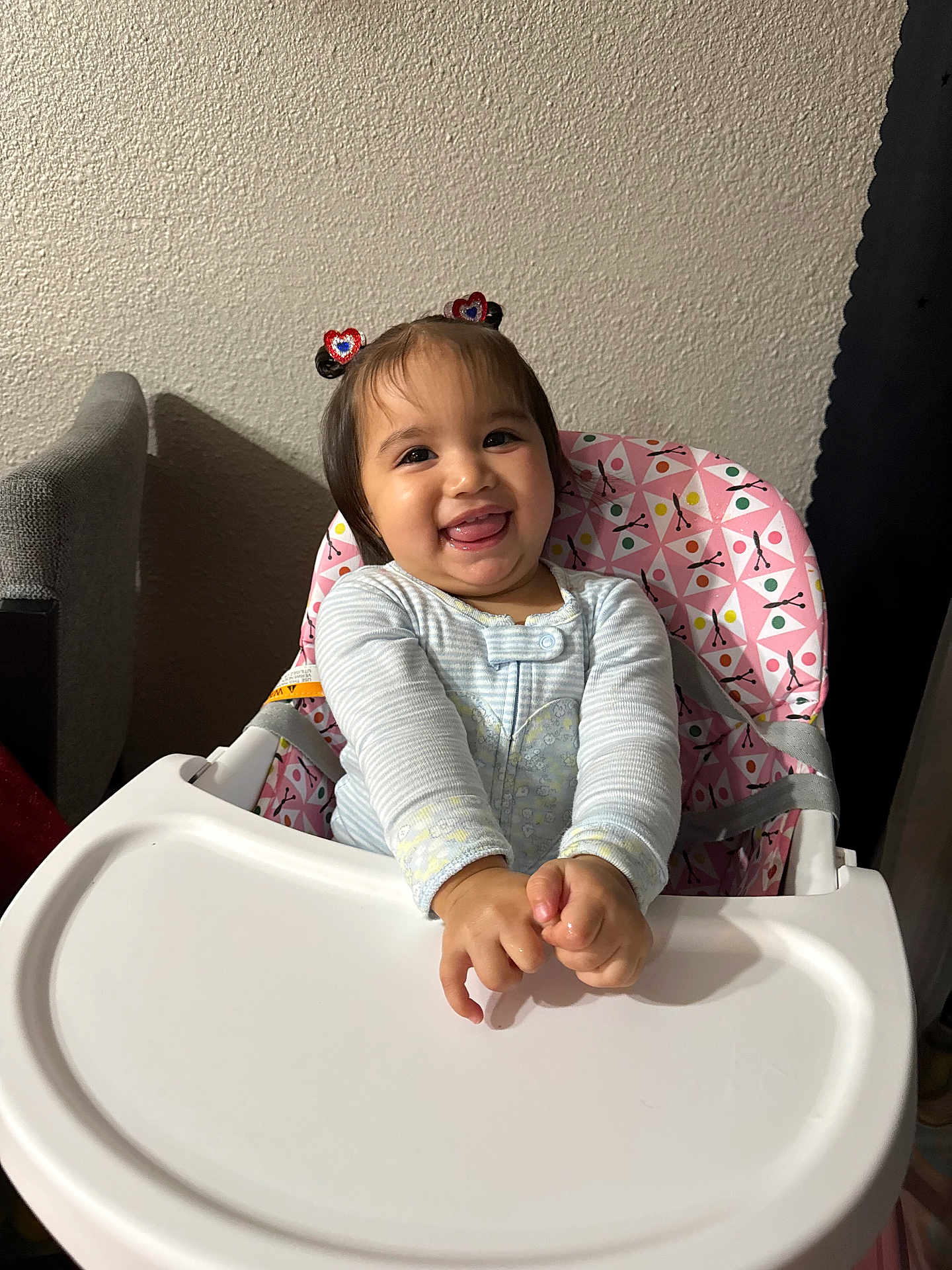 Maleya is registered to the contest to win money with this photo: baby, child, toddler, high_chair, pink, hair_clips, smiling, happy, indoor, cute, clothing, face, person, hands, tray, wall, pattern, seat, fun, playful