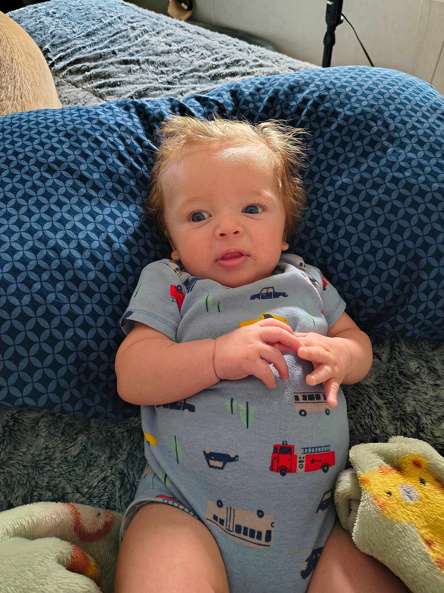 Benjamin is registered to the contest to win money with this photo: baby, blanket, blue_pillow, child, colorful, comfortable, cozy, curious, cute, hands, indoor, infant, legs, lying_down, onesie, patterned_clothing, person, sleeping_area, soft_texture, tousled_hair