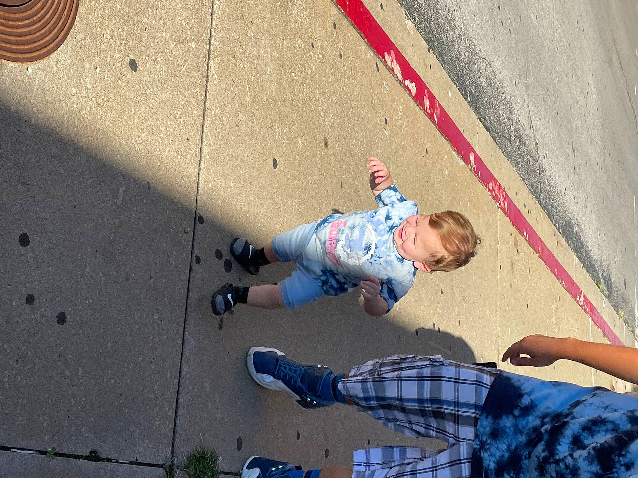 Ace is registered to the contest to win money with this photo: asphalt, child, city, concrete, footwear, fun, human_leg, knee, leg, leisure, pattern, pedestrian, person, recreation, road, road_surface, shadow, sidewalk, sitting, sneakers