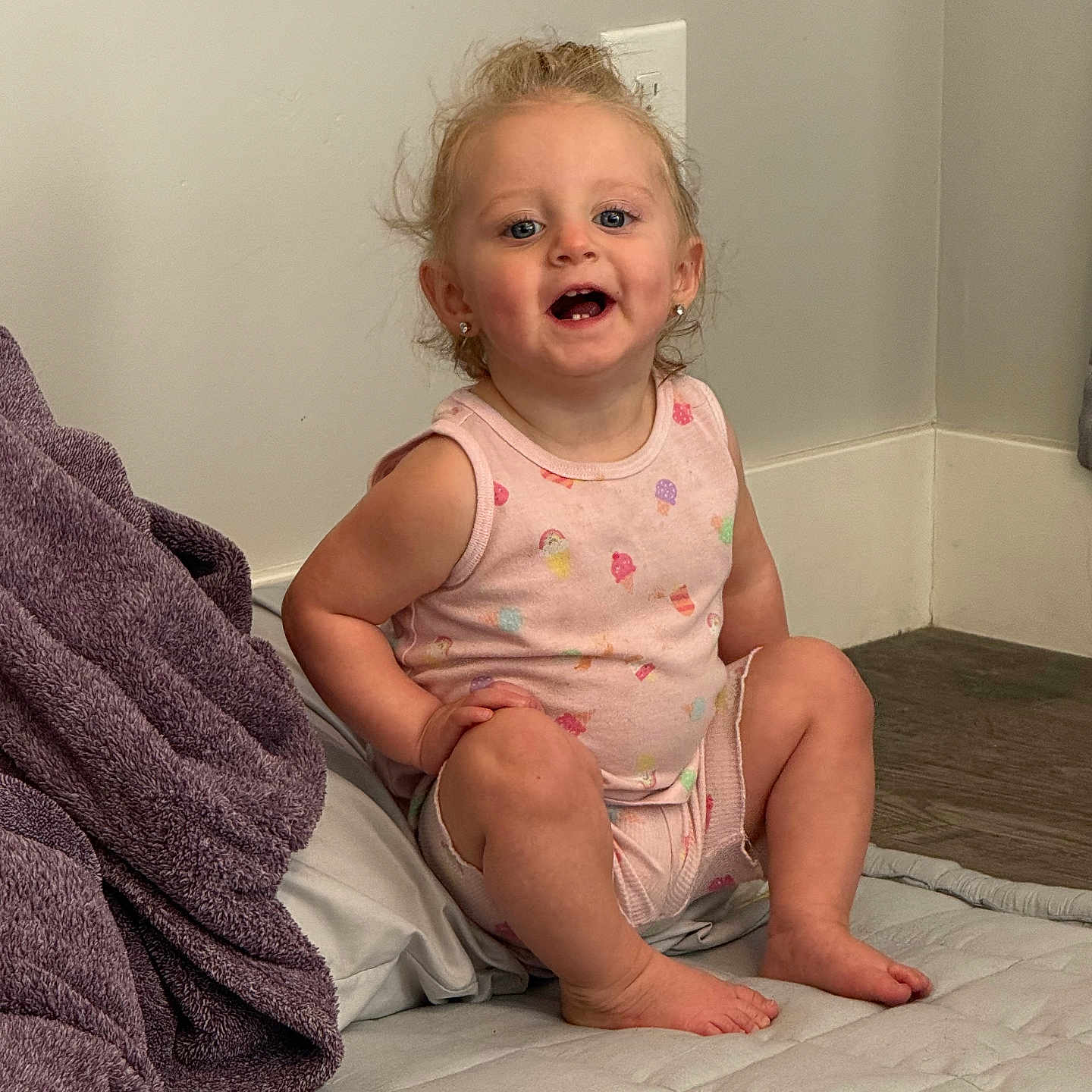 Glacier is registered to the contest to win money with this photo: baby, barefoot, blanket, casual, child, curly_hair, cute, earrings, floor, happy, indoors, light_switch, mattress, pink_clothing, portrait, sitting, smiling, toddler, wall, young_child