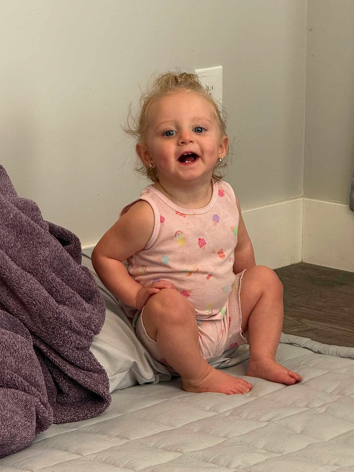 Glacier is registered to the contest to win money with this photo: baby, barefoot, blanket, casual, child, curly_hair, cute, earrings, floor, happy, indoors, light_switch, mattress, pink_clothing, portrait, sitting, smiling, toddler, wall, young_child