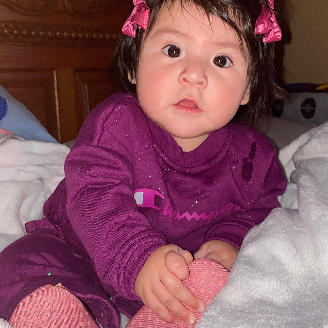 Zeynep joined the competition — help win amazing prizes! baby, bed, blanket, child, cozy, curious, dark_hair, face, hands, homedecor, indoor, pajamas, person, pink_bows, pink_slippers, portrait, sitting, soft_lighting, wide_eyes, wooden_headboard