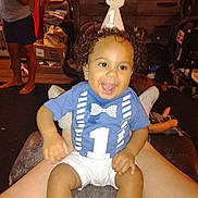 Izaiah joined the competition — help win amazing prizes! background, birthday, casual_clothing, celebration, child, curly_hair, footwear, furniture, happy, indoor, legs, party_hat, person, room, shirt, shorts, sitting, smiling, toddler, toy