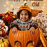 child, toddler, baby, smiling, portrait, halloween, pumpkin, jack_o_lantern, autumn, fall, costume, sweater, orange, cozy, fairy_lights, blankets, gourds, leaves, indoors, seasonal