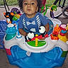 activity_walker, baby_toys, bicycle, blue_clothing, child, colorful, concrete, curious, curly_hair, cute, fun, grass, outdoor, person, play, smiling, toddler, toy_fish, toy_pandas, toy_penguin
