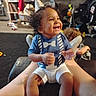 blue_shirt, bow_tie_design, candid, casual_clothing, child, clapping, curly_hair, furniture, happy, home, indoor, joyful, legs, living_room, person, shoes, smiling, toddler, toys, white_shorts
