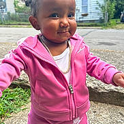 Laelani is registered to the contest to win money with this photo: toddler, child, baby, portrait, smiling, outdoor, pink_tracksuit, hoodie, sweatpants, gold_chain, standing, face, curly_hair, braids, residential_street, houses, sidewalk, daylight, fashion, happy