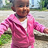 baby, braids, child, curly_hair, daylight, face, fashion, gold_chain, happy, hoodie, houses, outdoor, pink_tracksuit, portrait, residential_street, sidewalk, smiling, standing, sweatpants, toddler