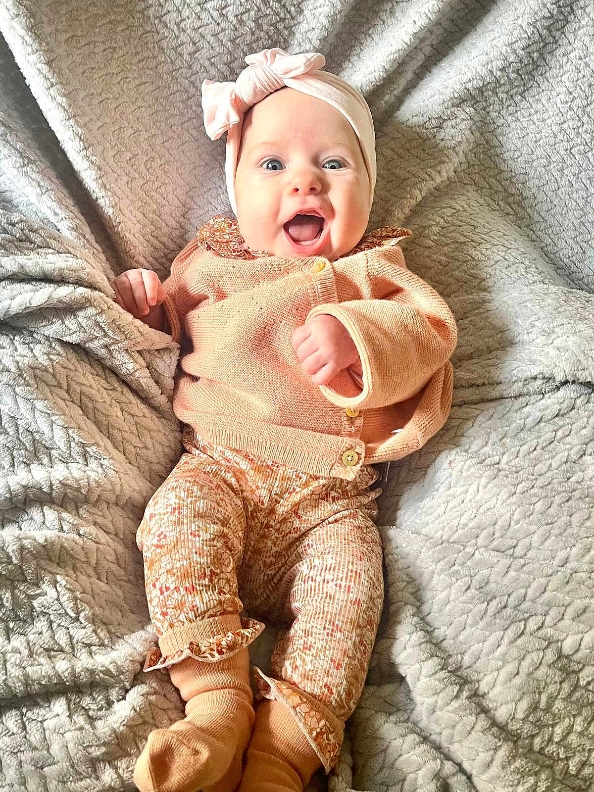 élyana a rejoint le concours — aidez-le/la à gagner de superbes lots ! baby, infant, smiling, headband, bow, cozy_clothing, blanket, soft_texture, patterned_pants, socks, happy, cute, child, portrait, indoor, laying_down, warm_colors, knitwear, expression, small_hands