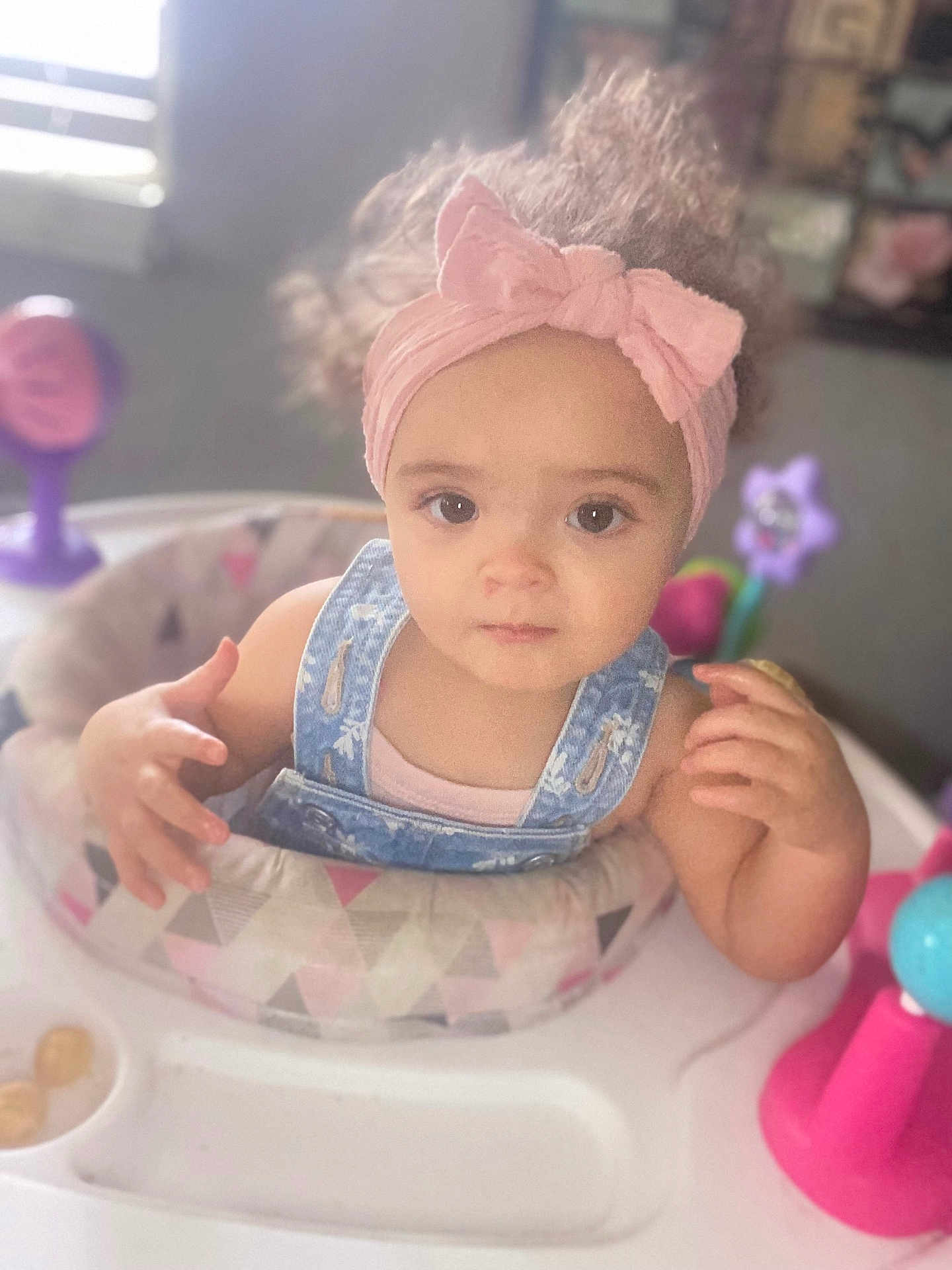 Leinani joined the competition — help win amazing prizes! toddler, baby, child, headband, pink, denim_overalls, curly_hair, activity_center, toy, indoor, natural_light, face, hands, exploring, cute, expression, young_child, play, colorful, window_light