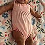 arms, baby, blanket, child, cozy, cute, face, floral_pattern, happy, indoors, infant, legs, lying_down, mittens, pink_outfit, portrait, skin, smiling, soft_texture, young_child