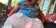Harmoniee is registered to the contest to win money with this photo: baby, child, tutu, dress, blue_top, pink, flower, porch, outdoor, person, tricycle, curly_hair, smiling, happy, holding, legs, window, railing, daylight, casual
