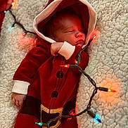 Puku is registered to the contest to win money with this photo: baby, newborn, sleeping, red_clothing, hoodie, santa_outfit, blanket, christmas_lights, festive, holiday, cozy, infant, cute, soft_texture, warm_lighting, holiday_season, portrait, indoors, peaceful, closeup