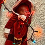 baby, newborn, sleeping, red_clothing, hoodie, santa_outfit, blanket, christmas_lights, festive, holiday, cozy, infant, cute, soft_texture, warm_lighting, holiday_season, portrait, indoors, peaceful, closeup