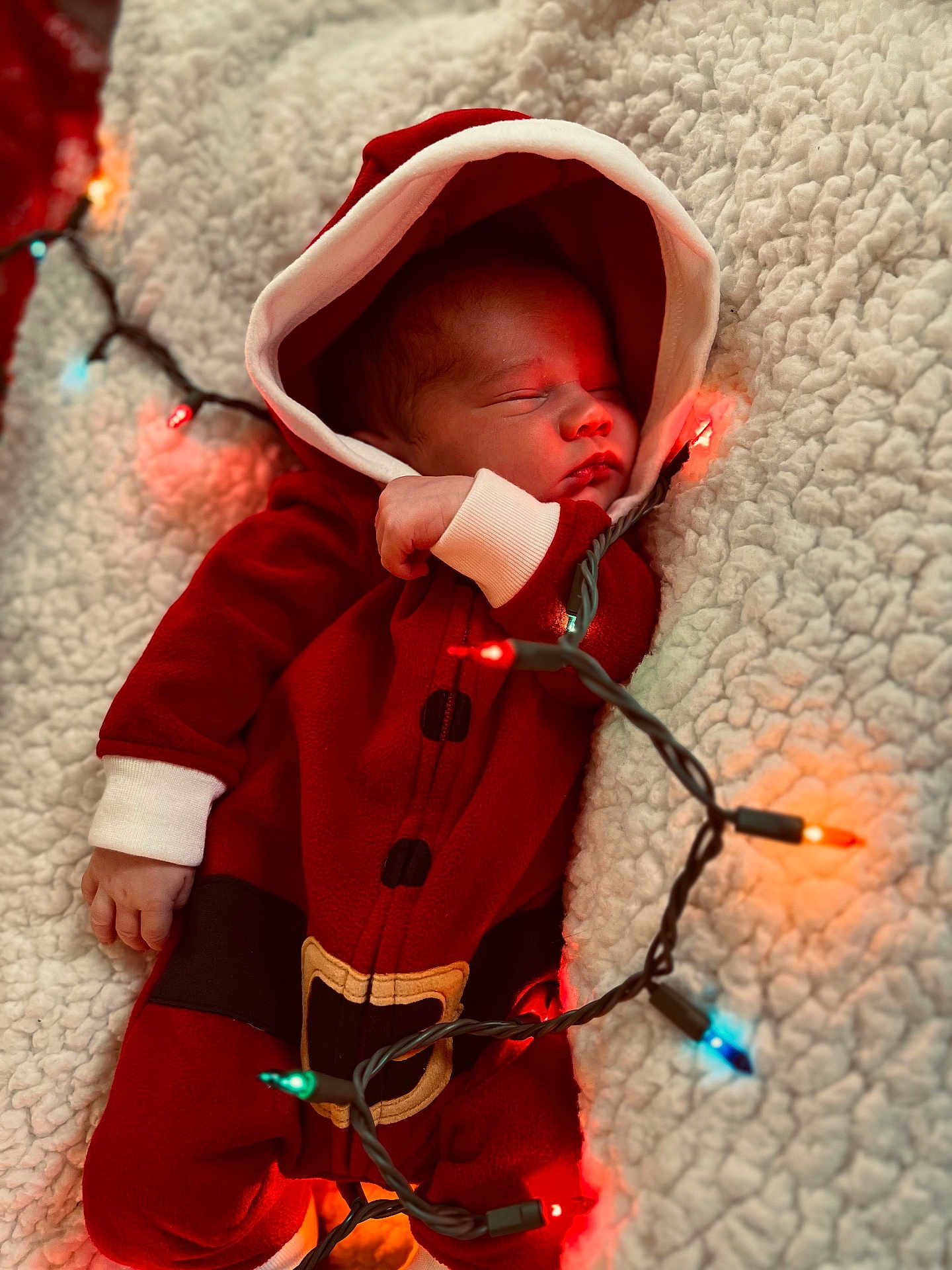 Puku is registered to the contest to win money with this photo: baby, newborn, sleeping, red_clothing, hoodie, santa_outfit, blanket, christmas_lights, festive, holiday, cozy, infant, cute, soft_texture, warm_lighting, holiday_season, portrait, indoors, peaceful, closeup