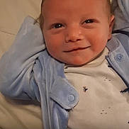 Jameson is registered to the contest to win money with this photo: baby, infant, smile, face, blue_jacket, white_shirt, lying_down, closeup, child, cute, relaxed, cozy, indoors, portrait, small_prints, skin, hair, expression, young, person