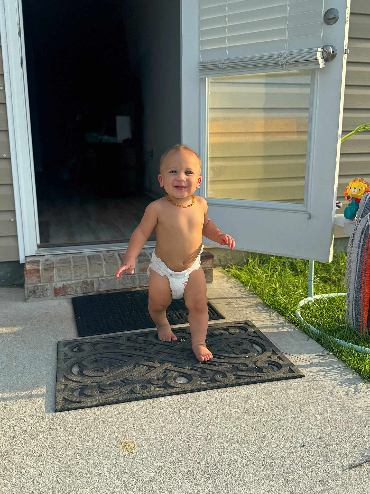 Carter joined the competition — help win amazing prizes! toddler, child, diaper, smile, outdoor, door, doormat, sunlight, grass, concrete, necklace, house, brick, shadow, foot, hand, toy, window_blind, happy, person